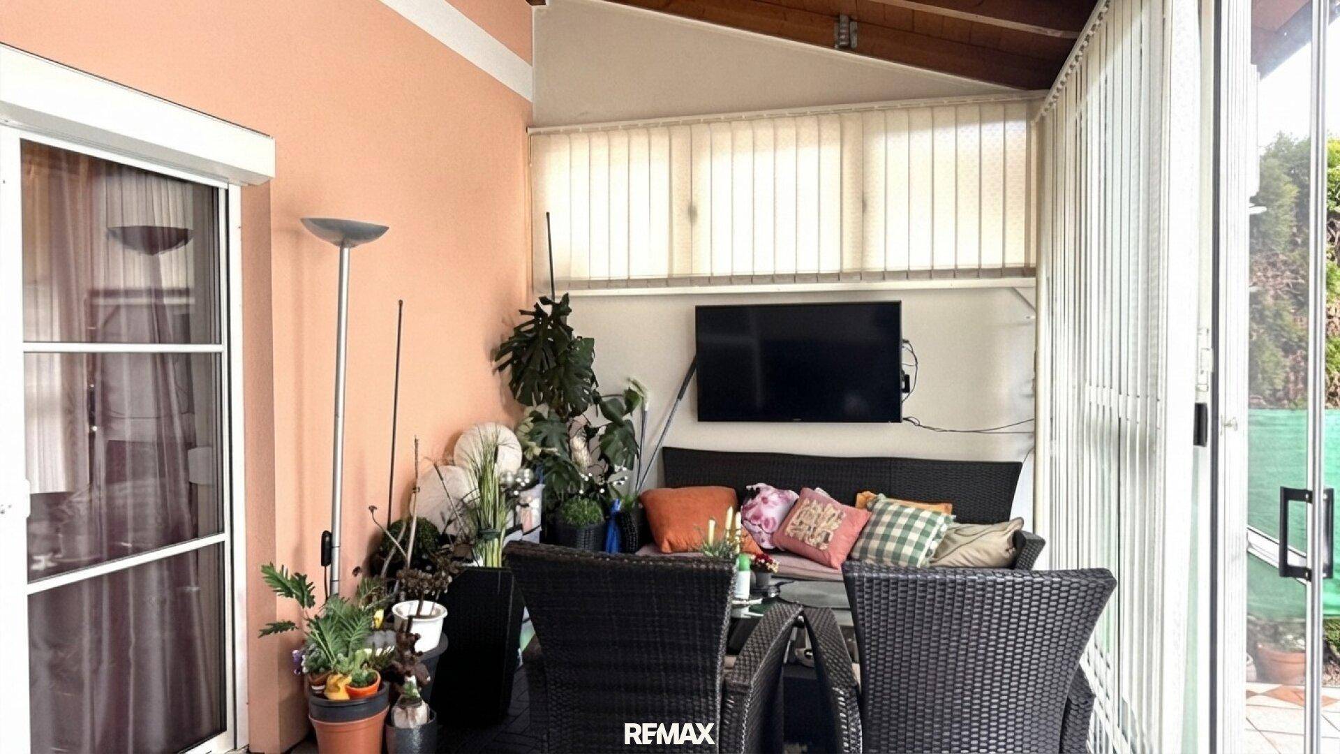 Gemütlicher Wintergarten mit Sitzgelegenheiten, Fernseher und vielen Pflanzen, ideal zum Entspannen.
