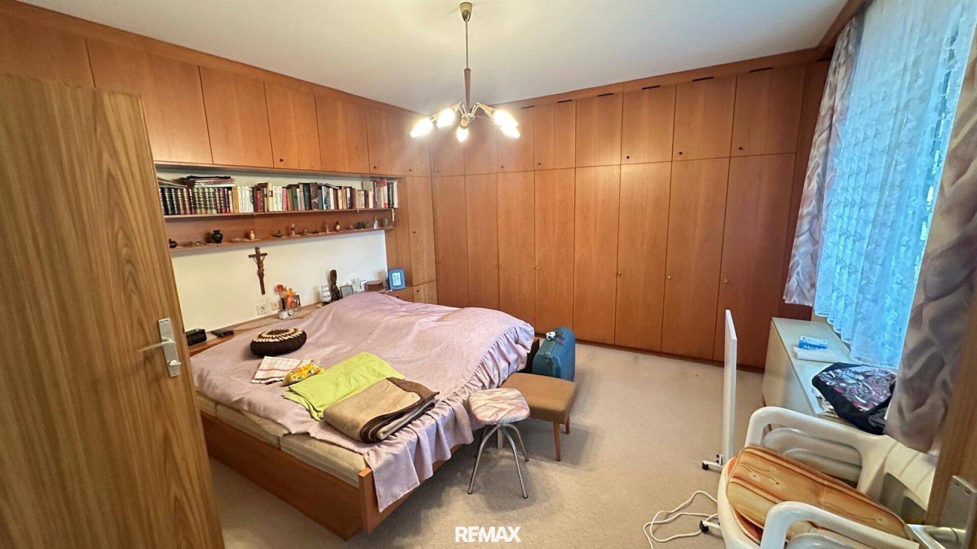Schlafzimmer mit Holzeinbauschränken, Doppelbett und Fenster mit Vorhängen, gemütlich eingerichtet.