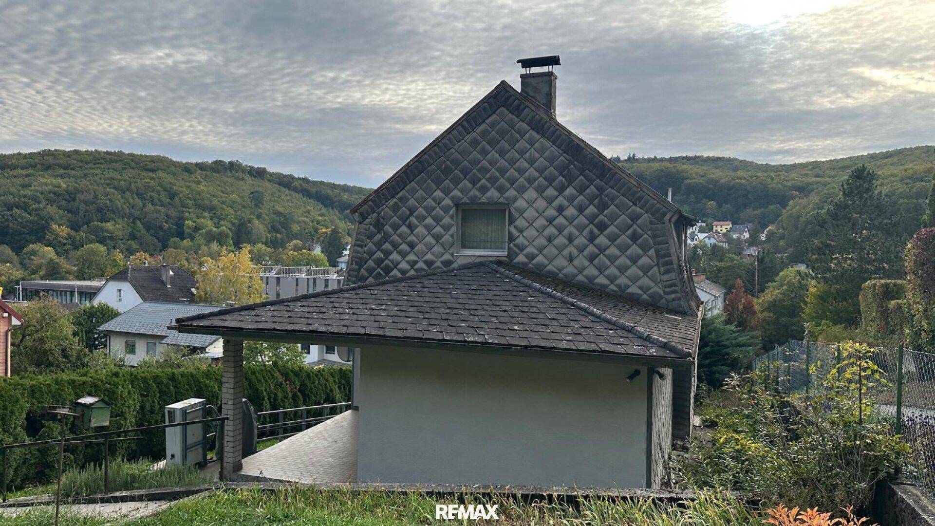 Rückansicht des Hauses mit Schieferdach und Blick auf die bewaldete Hügellandschaft.