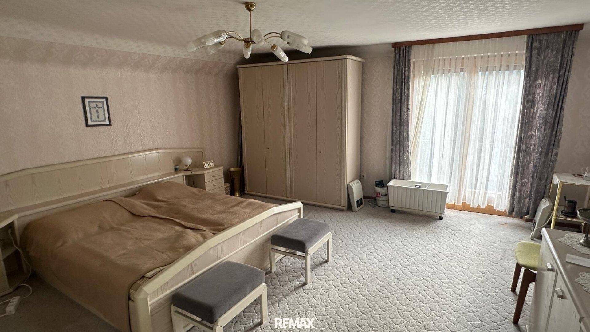 Helles Schlafzimmer mit Doppelbett, Teppichboden, großem Kleiderschrank und Balkonzugang.
