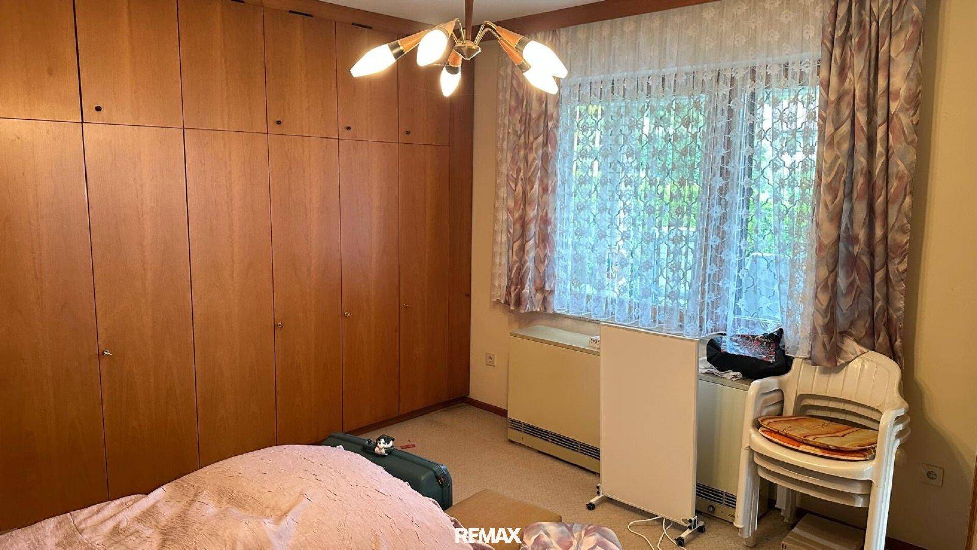 Schlafzimmer mit großen Holzeinbauschränken, Teppichboden und Fenster mit Vorhängen.