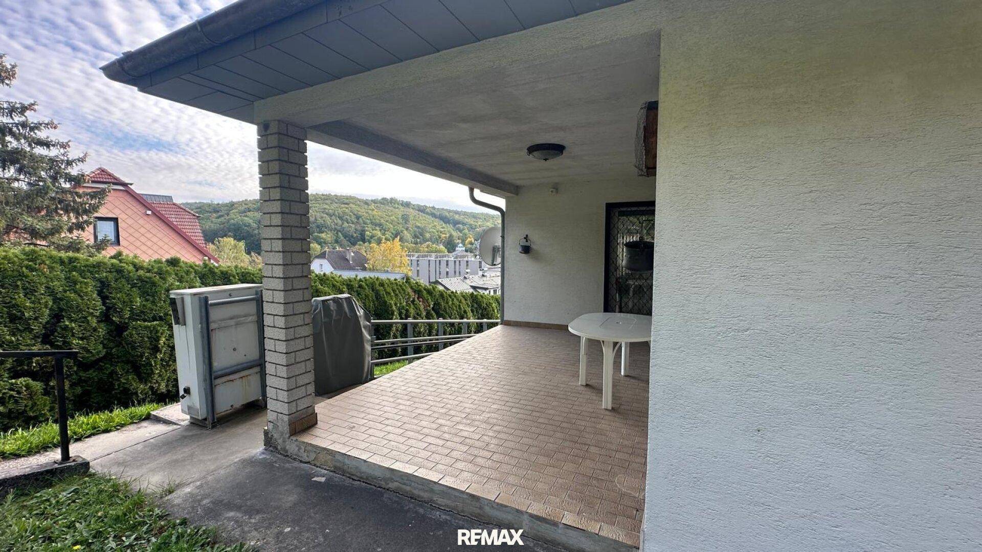 Geräumige überdachte Terrasse mit Fliesenboden und Ausblick auf die bewaldeten Hügel.