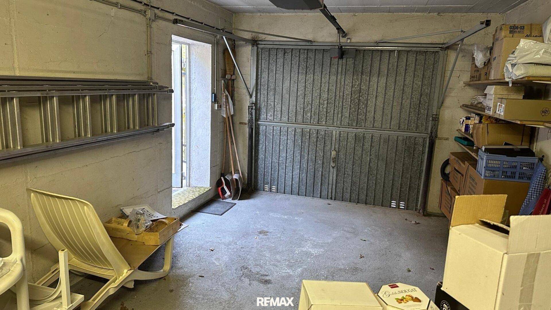Innenansicht der Garage mit Rolltor, Lagerregalen und verschiedenen Gegenständen.