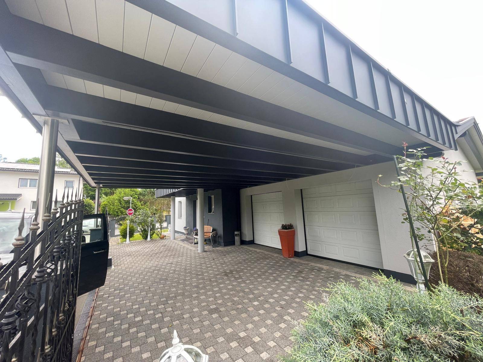 Geräumiger Carport mit gepflasterter Einfahrt und zwei Garagentoren für Fahrzeuge.