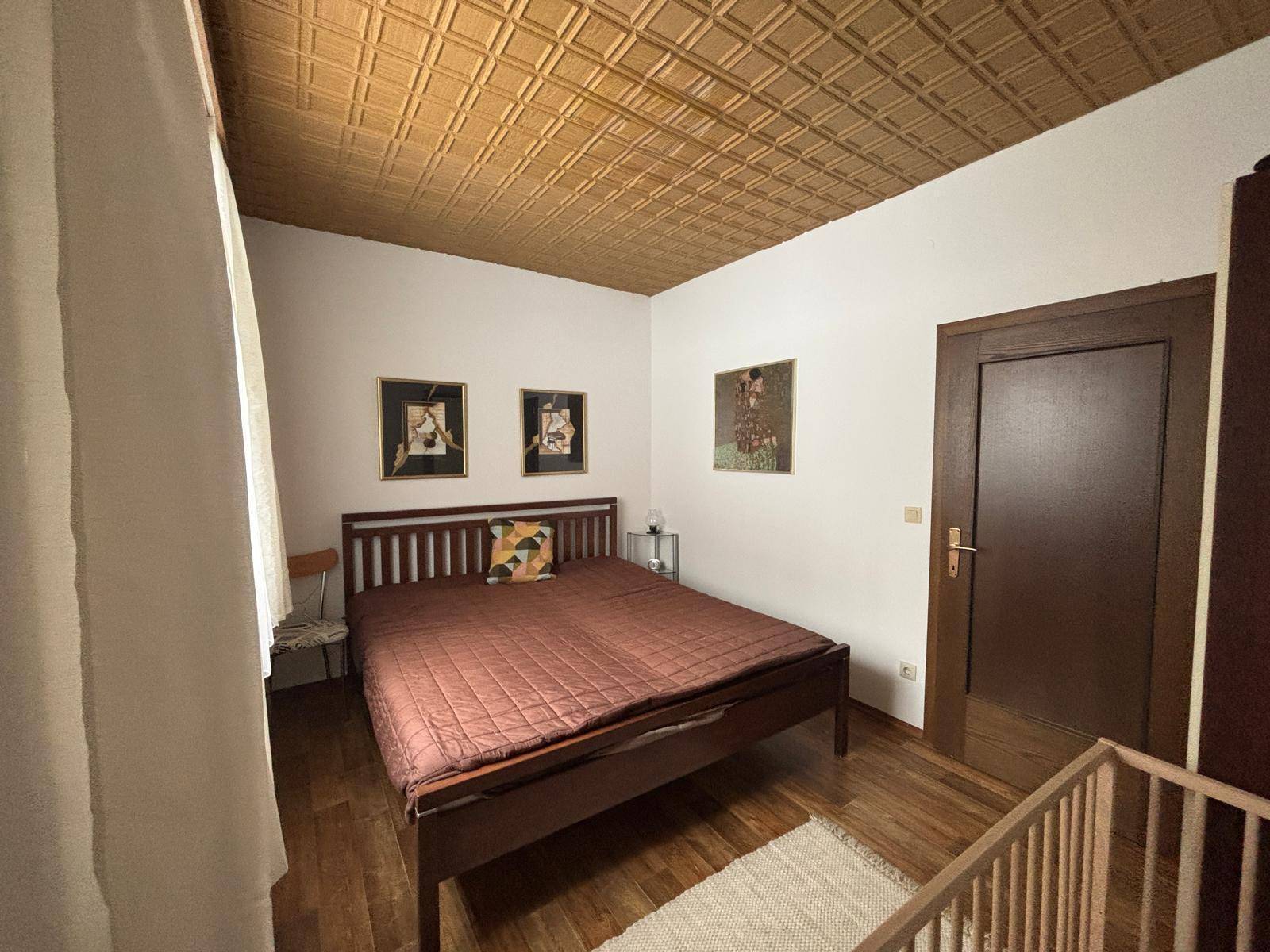 Schlafzimmer mit Holzbett, Parkettboden und einer auffälligen Holzdeckenverkleidung.