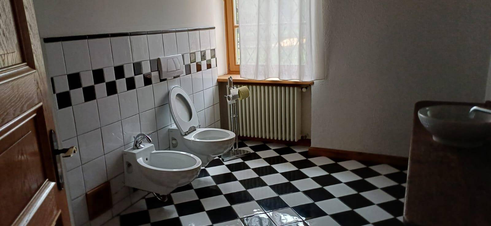 Badezimmer mit schwarz-weiß gefliestem Boden, Bidet, Toilette und Fenster für Tageslicht.