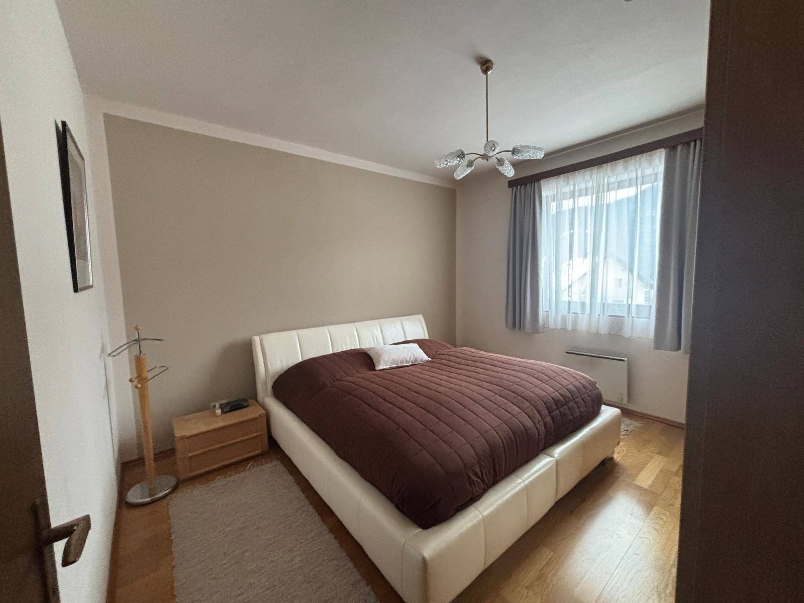 Helles Schlafzimmer mit modernem Doppelbett, Parkettboden und Fenster mit Vorhängen.