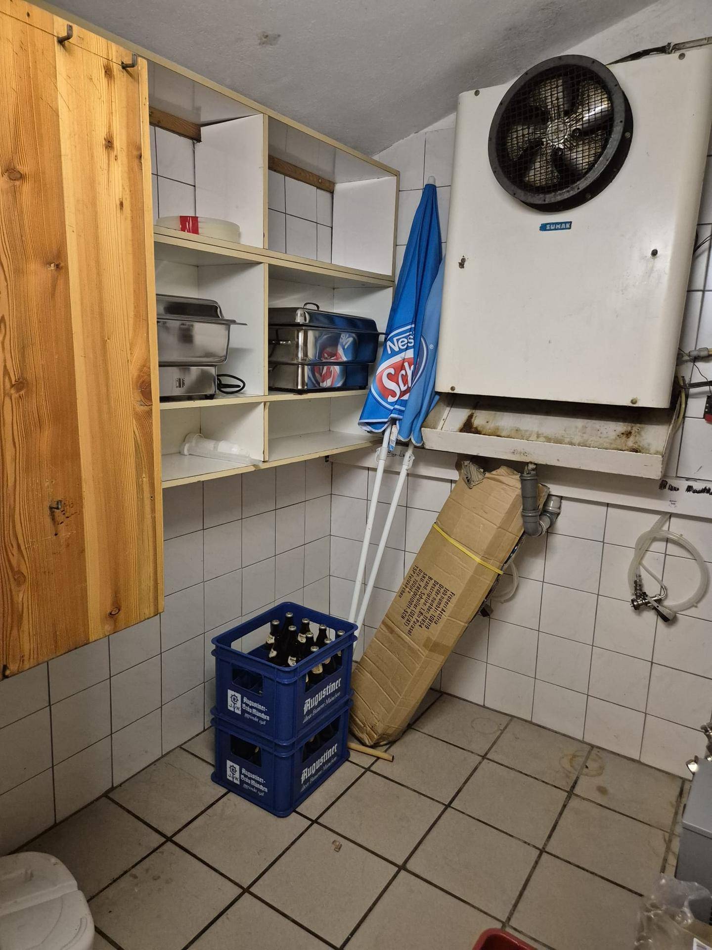 Lagerraum mit Regalen, Bierkästen und einer großen Lüftungsanlage an der gefliesten Wand.