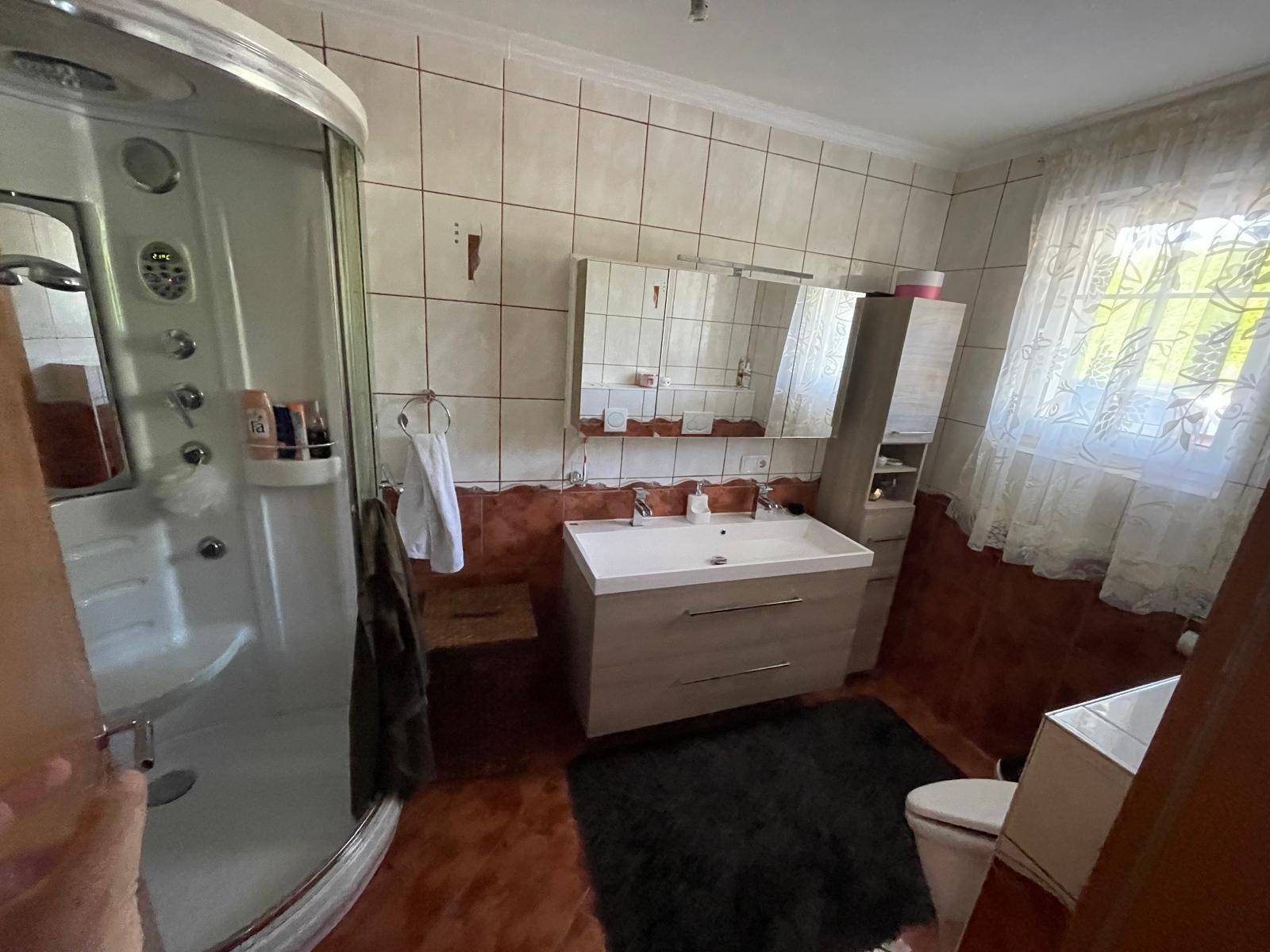Badezimmer mit Duschkabine, modernem Waschtisch und Fenster für Tageslicht.