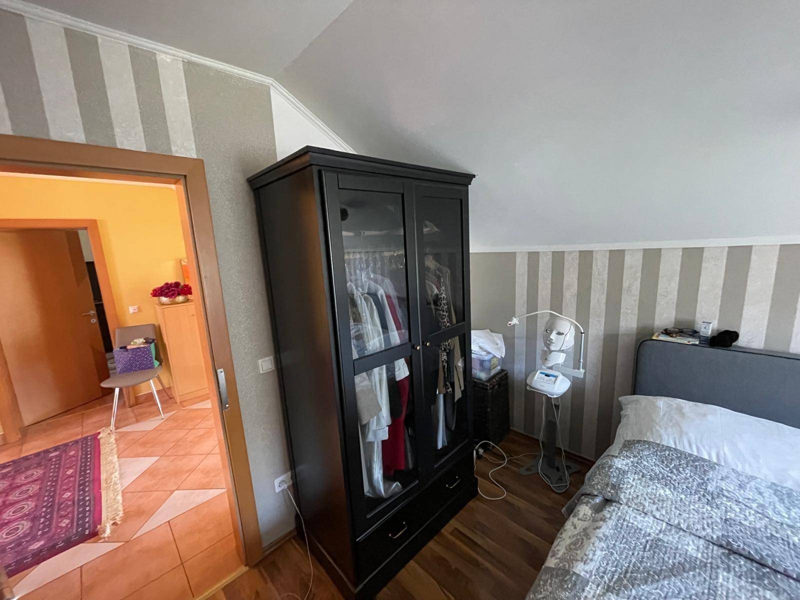Schlafzimmer im Dachgeschoss mit gestreifter Tapete, Laminatboden und Kleiderschrank.