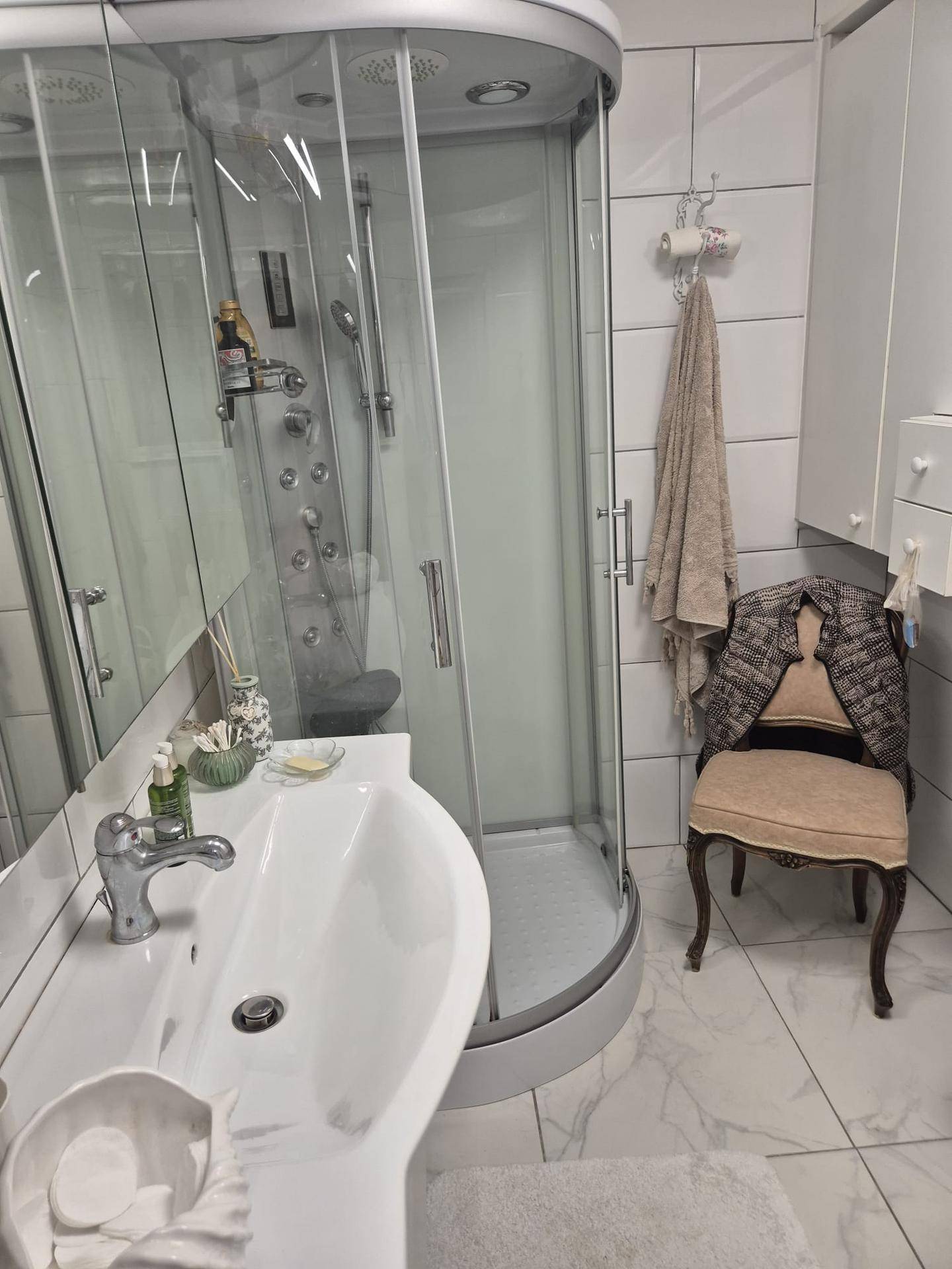 Modernes Badezimmer mit Duschkabine, Waschbecken und hell gefliesten Wänden und Boden.