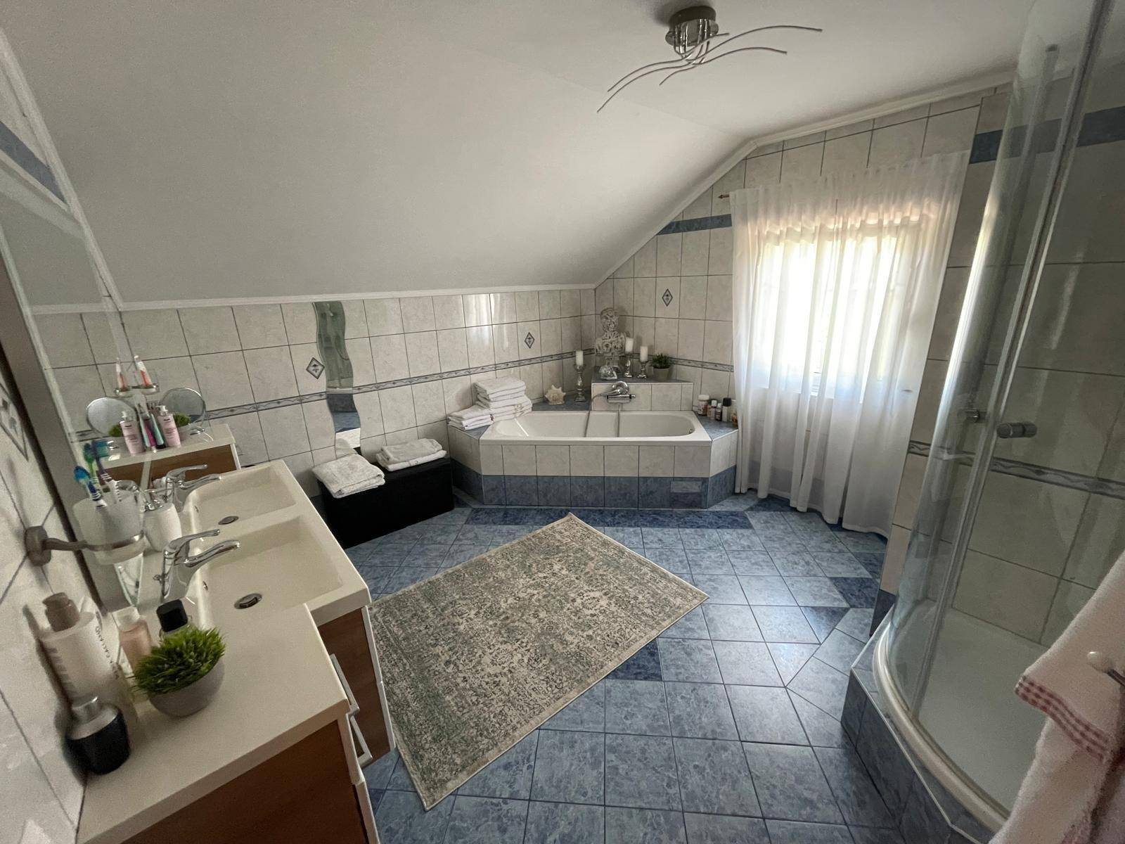 Geräumiges Badezimmer im Dachgeschoss mit Badewanne, Doppelwaschbecken und blauen Fliesen.
