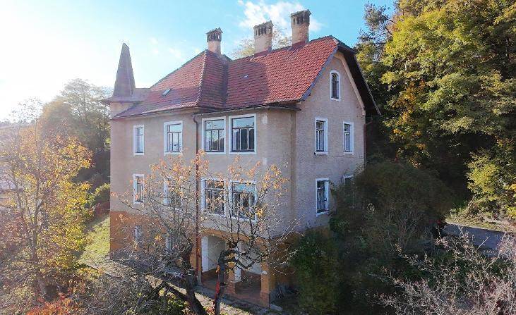 Ansicht der historischen Villa mit mehreren Schornsteinen und herbstlicher Baumkulisse.