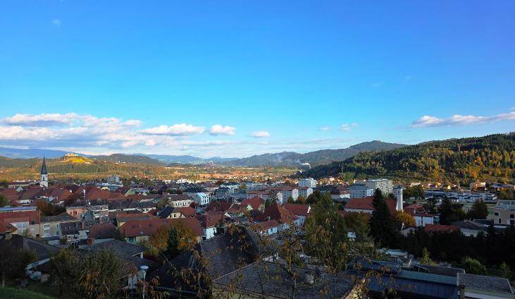 Panoramablick über die Stadt mit ihren Dächern und den dahinterliegenden bewaldeten Bergen.