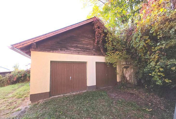 Separate Doppelgarage mit Holztoren und einem Satteldach, umgeben von Vegetation.