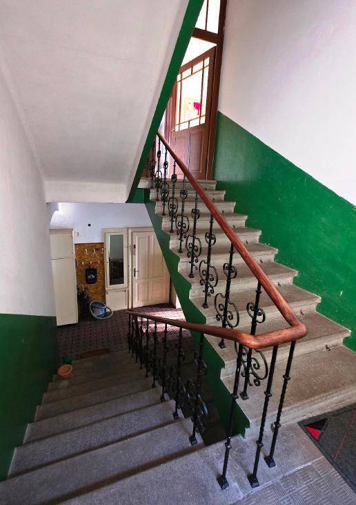 Treppenhaus mit grün gestrichenen Wänden, schmiedeeisernem Geländer und Holztüren.