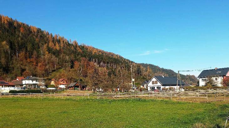 Panoramablick auf eine ländliche Siedlung am Fuße eines bewaldeten Hügels mit Herbstfarben.