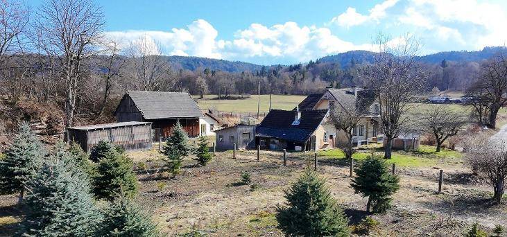 Ländliches Anwesen mit mehreren Gebäuden, umgeben von Bäumen und Hügeln unter blauem Himmel.