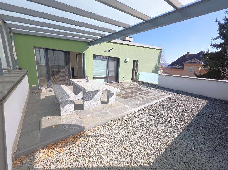 Geräumige Terrasse mit Steinfliesen, Kiesbereich und einem festen Steintisch unter einer Pergola.