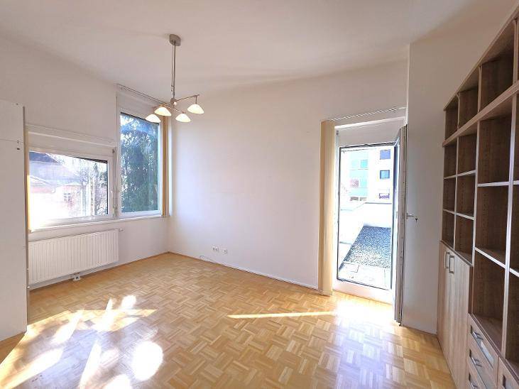 Heller Raum mit Parkettboden und Zugang zu einem Außenbereich, ideal als Wohn- oder Arbeitszimmer.