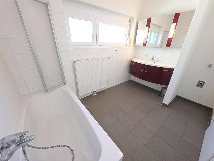 Helles Badezimmer mit Badewanne, modernem Waschtisch und Fenster für natürliche Belüftung.