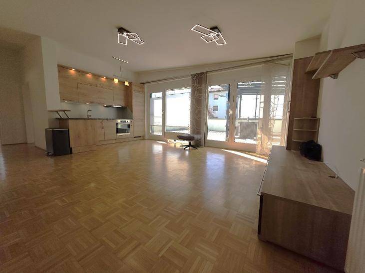 Offener Wohnbereich mit Parkettboden, integrierter Küchenzeile und Zugang zu einem Balkon.