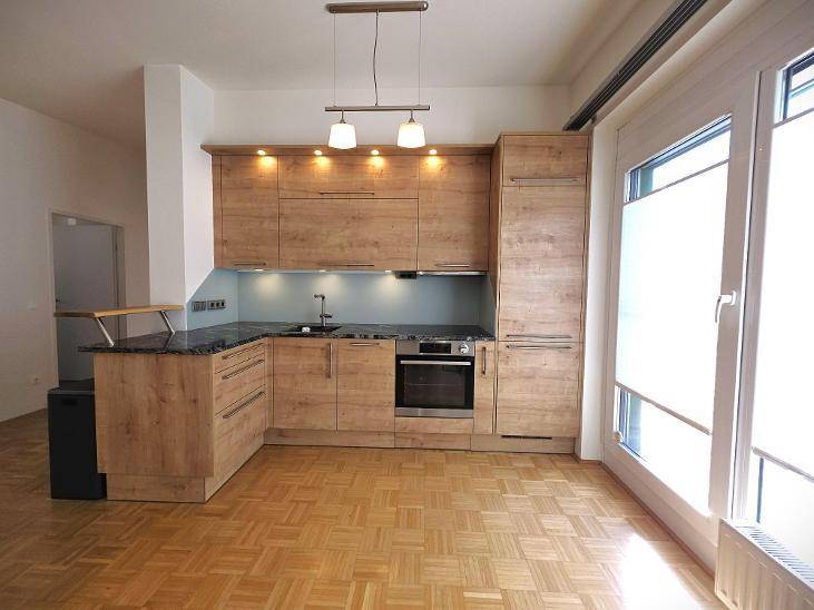 Moderne Einbauküche mit Holzfronten, dunkler Arbeitsplatte und Parkettboden, gut beleuchtet.