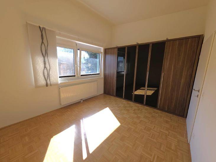 Schlafzimmer mit Parkettboden, großem Fenster und integriertem Kleiderschrank, hell und freundlich.