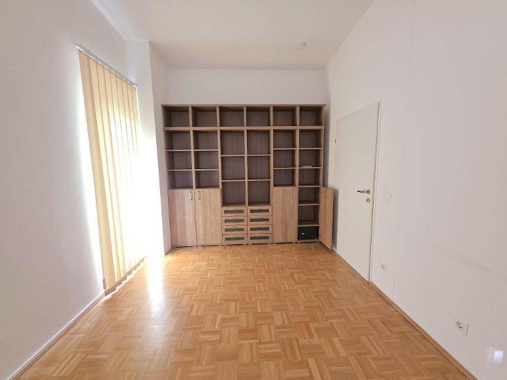 Geräumiger Raum mit Parkettboden und einer großen Bücherwand, ideal als Büro oder Bibliothek.