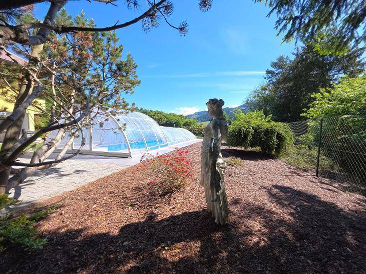 Außenpool mit Überdachung, umgeben von einem gepflegten Garten mit dekorativer Statue.