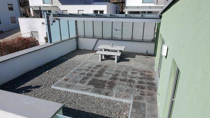 Geräumige Terrasse mit Steinplatten, Kiesbereich und einer Sitzgruppe unter einer Überdachung.