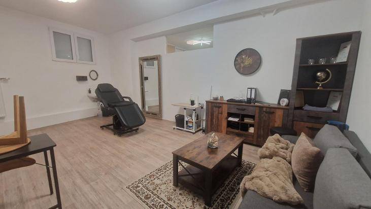 Geräumiger Innenraum mit Holzboden, einer Behandlungsliege, einem Sofa und rustikalen Holzmöbeln.