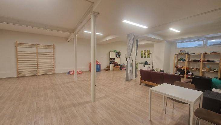 Großer Mehrzweckraum mit Holzboden, Sprossenwand und mehreren Stützpfeilern.