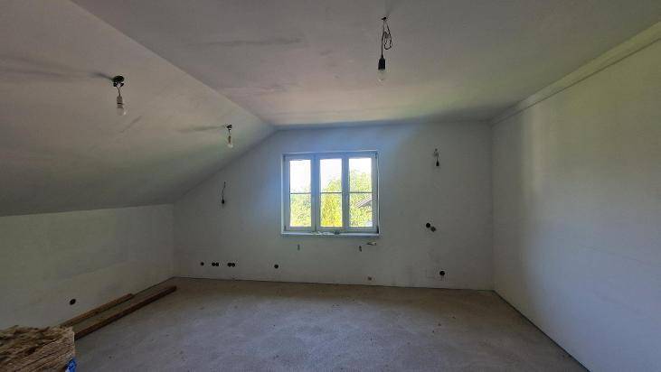 Unfertiger Dachbodenraum mit schräger Decke und einem Fenster, bereit für den Ausbau.