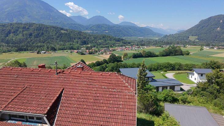 Aussicht über das rote Ziegeldach des Hauses auf das weite Tal und die umliegenden Berge.