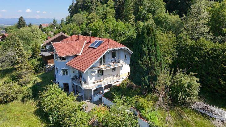 Luftaufnahme eines Hauses mit rotem Ziegeldach, Solarpaneelen und mehreren Balkonen, umgeben von Bäumen.