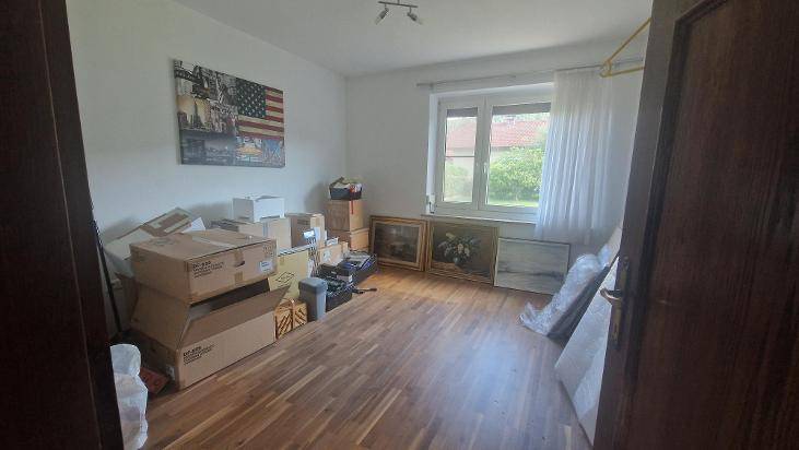 Helles Zimmer mit Holzboden, gefüllt mit Umzugskartons und Bildern, bereit zur Einrichtung.