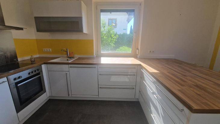 Funktionale Küche mit weißen Fronten, Holz-Arbeitsplatten, Spüle und integriertem Backofen.