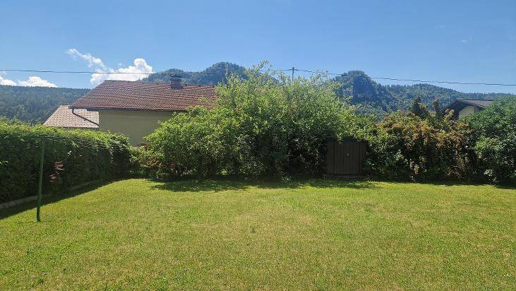 Großer Garten mit Rasenfläche, umgeben von Hecken und einem kleinen Geräteschuppen mit Bergblick.