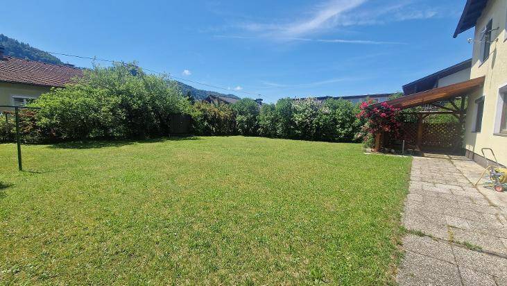 Ausgedehnte Rasenfläche im Gartenbereich mit Blick auf das Haus und den überdachten Eingang.