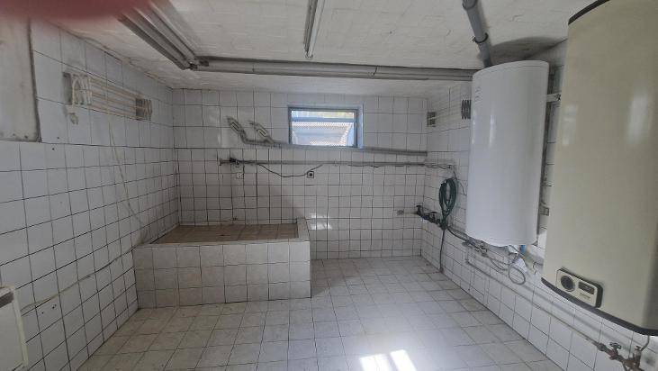 Gefliester Hauswirtschaftsraum im Keller mit Wasseranschlüssen und Warmwasserboiler.