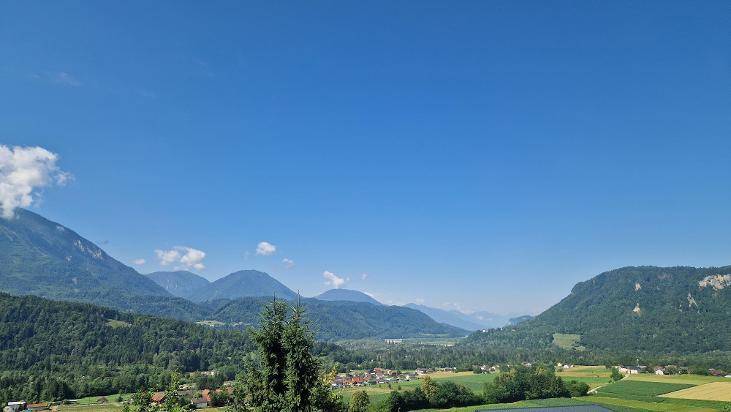 Weitläufiger Panoramablick über ein grünes Tal mit majestätischen Bergen unter blauem Himmel.