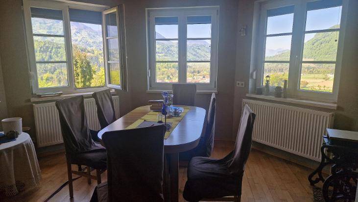 Heller Essbereich mit Holztisch und Stühlen, großen Fenstern und Bergblick.
