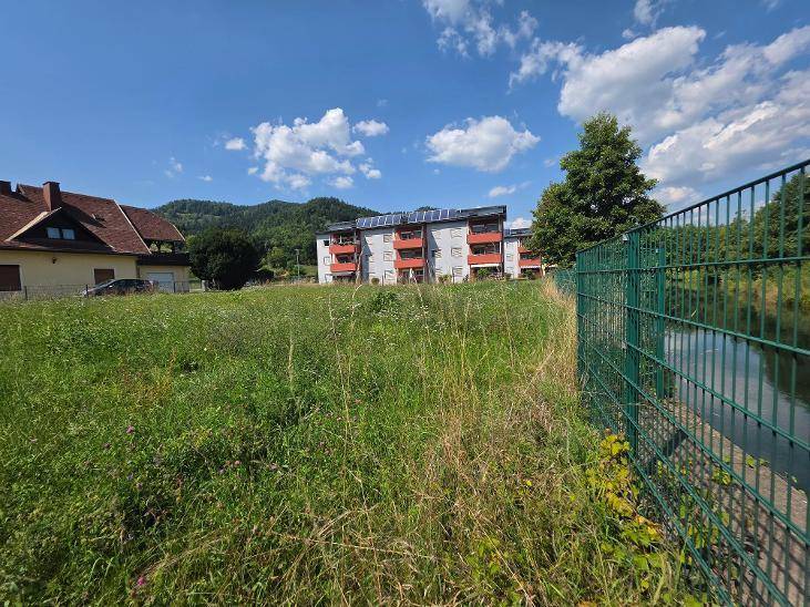 Grüne Wiese mit Blick auf ein Wohnhaus mit Solaranlagen und einen angrenzenden Wasserlauf.