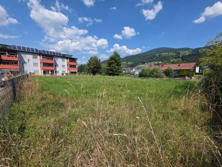 Großes grünes Feld neben einem modernen Wohngebäude mit Solaranlagen und Bergpanorama.