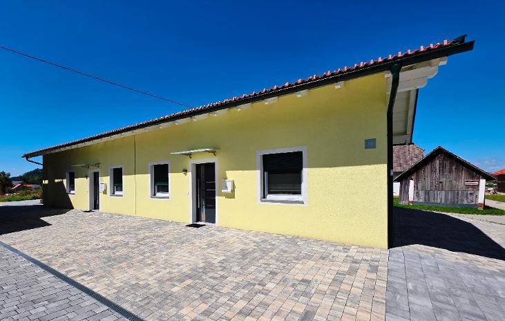 Seitenansicht eines modernen gelben Hauses mit großen Fenstern und gepflastertem Zugangsbereich.