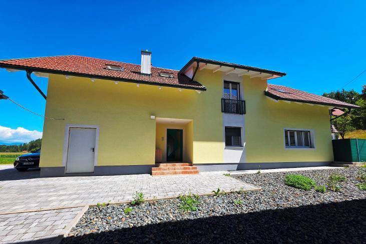 Gelbes Einfamilienhaus mit rotem Ziegeldach, kleinem Balkon und gepflastertem Vorplatz.
