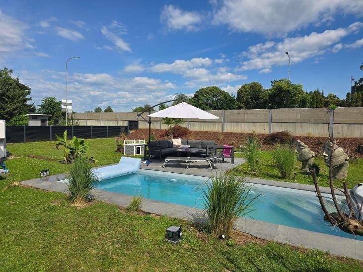 Weitläufiger Garten mit großem Pool, Sonnenschirm und Lounge-Möbeln unter blauem Himmel.