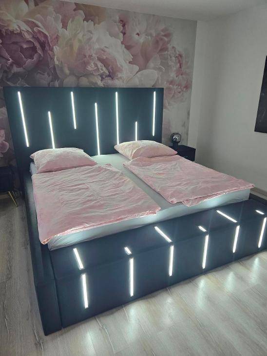 Modernes Schlafzimmer mit beleuchtetem Bettrahmen und einer floralen Akzentwand.