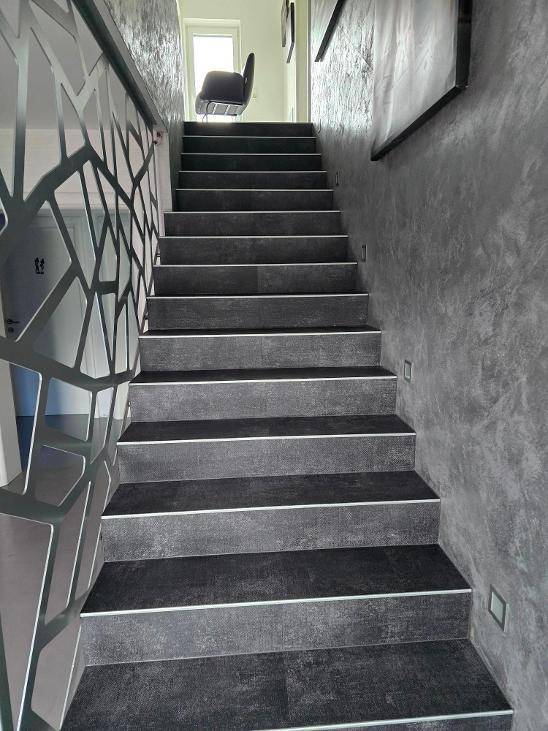 Moderne Treppe mit dunklen Stufen, beleuchteten Akzenten und einem dekorativen Geländer.